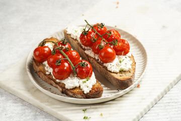 a sandwich with roasted cherry tomatoes with branch, fresh cottage cheese, green basil on a slice of whole wheat bread on a round plate on marble tray on grey background