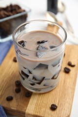 Glass of milk with grass jelly and coffee beans on wooden board, closeup