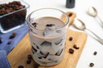Glass of milk with grass jelly and coffee beans on white table, closeup