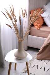 Vase with decorative dried plants on table in bedroom. Interior design