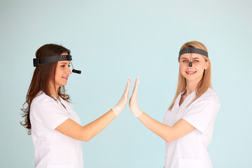 Two female otolaryngologists are happy with the work they have done and clap their hands on a light background. Health protection concept