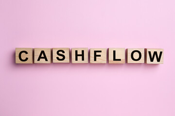 Wooden cubes with phrase Cash FLow on pink background, flat lay