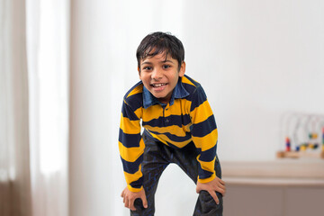 An Indian boy bending forward and looking At Camera