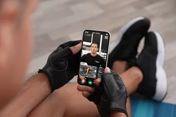 Tuinposter Man having workout with personal trainer via smartphone at home, closeup © New Africa