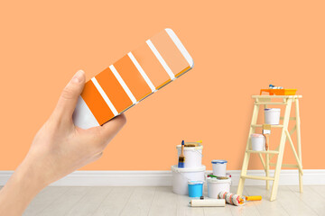 Decorator holding color palette samples in room with painted wall, closeup. Interior renovation