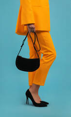 Fototapeta na wymiar Young woman wearing stylish orange clothes with bag on light blue background, closeup