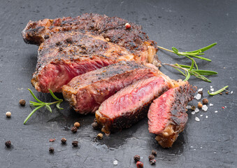 Grilled medium rare ribeye steak on gray stone plate.