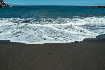 Ocean foam covering wonderful black sand beach of Tenerife island.