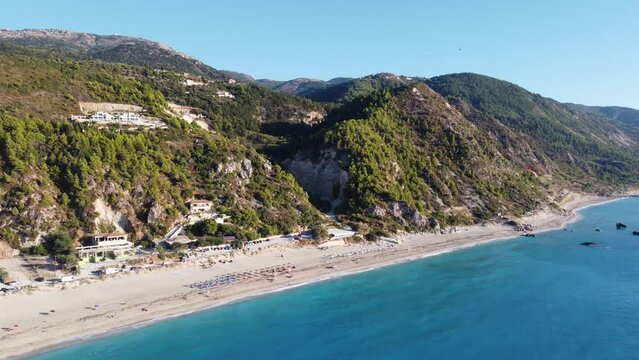 Aerial view of beautiful sandy beach with sunshades and soft turquoise ocean wave. Para glider is flying over tropical sea in summer season on Kathisma beach on Lefkada island.