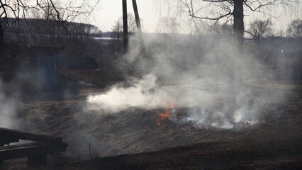 Smoked burning dry grass near rural barn at spring day. Danger of fire