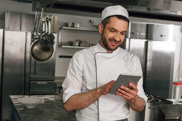 Smiling chef in uniform making order in digital tablet for the supplier standing on kitchen