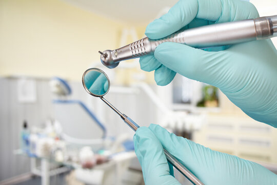 Dentist's hands in gloves with dental handpiece and mouth mirror.