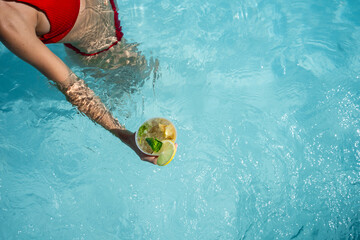 Woman in red bikini taking a mojito cocktail in the swimming pool in summer