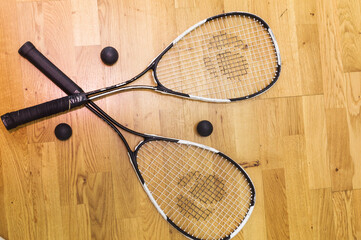 Two rackets and two squash balls lie on the parquet floor