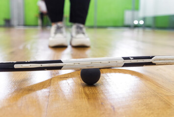 A black squash ball lies under a tennis racket on a parquet floor