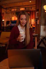 Pretty blond woman sit in cafe, drink coffee or tea  and working on laptop