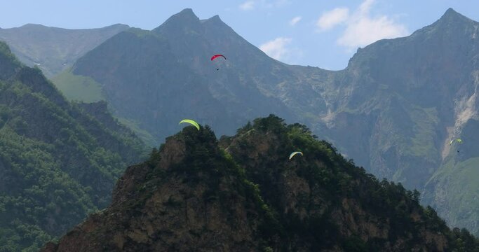 Paragliding pilots fly paragliders among clouds and green mountains.