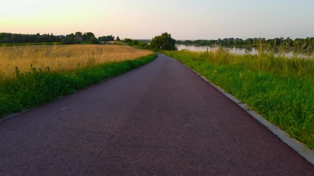 POV of professional cyclist riding along beautiful rural bike path between fields and river. Light workout or strength training on sunny summer evening. Concept healthy lifestyle and outdoor exercise
