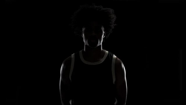 Portrait of a basketball player. Sidelit African American man in sports uniform posing against black background.