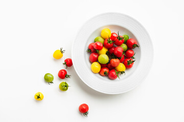 Naklejka na ściany i meble Colorful cherry tomatoes in organic red, yellow and green are served on a white round plate. The concept is to eat ripe vegetables neatly. Vegetarian diet space, flat top view.