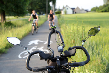 Kierownica roweru, para ludzi jedzie na rowerach ścieżką rowerową. - obrazy, fototapety, plakaty
