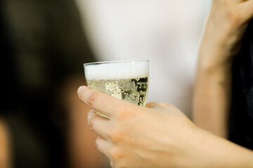 Shallow depth of field (selective focus) details with the hand of a woman holding a plastic glass of champagne or sparkling wine.
