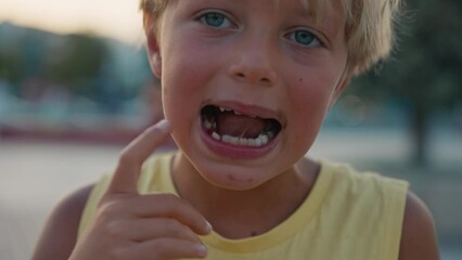  a small boy with blond hair with showing his milk tooth opening his mouth to show where he lost one of his baby's milk tooth while eating ice cream. High quality 4k footage