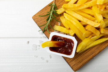 French fries with ketchup tomato sauce on a wooden background. Fast food. Baked homemade potatoes with rosemary. Harmful food. Place for text. Copy space.