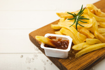 French fries with ketchup tomato sauce on a wooden background. Fast food. Baked homemade potatoes with rosemary. Harmful food. Place for text. Copy space.