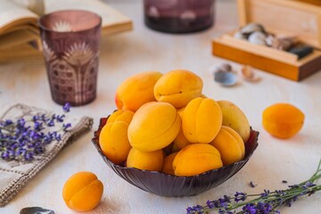 Ripe juicy apricots in a burgundy glass bowl on a light concrete background. Vintage style.