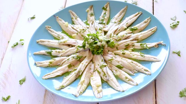 Pickled anchovies with garlic and parsley marinated in vinegar in a round wooden plate on a white wooden table. Typical Spanish snack. 