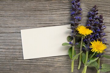 White blank card for mockup near yellow and violet flowers on natural grey wooden background.