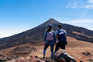 Hiking couple with backpacks holding hand on summit Pico Viejo with scenic view on the peak of volcano Pico del Teide, Tenerife, Canary Islands, Spain, Europe. Volcanic barren solidified lava terrain © Chris