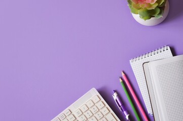 Computer keyboard, pen, pencils, paper notebook and cactus on a purple background. Office or school table top view photography, flat lay composition