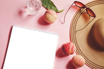 Summer lifestyle photo. White sheet of paper, juicy peaches, straw hat, sunglasses and a glass of water on a pink background. Holiday, travel concept