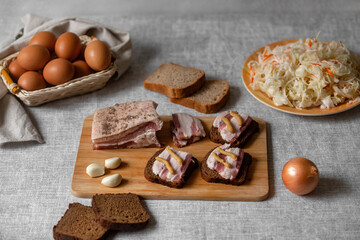 rustic natural food, on a linen tablecloth a wooden board, on it are ready-made sandwiches from black rye bread and lard with mustard and boiled eggs and sauerkraut