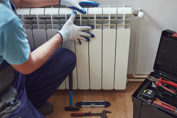 Central heating mechanic and handyman fixing home radiator, gas crisis and seasonal issues. - obrazy, fototapety, plakaty