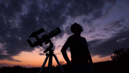 Man with astronomical telescope observing night sky, under the Milky way stars.