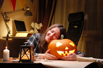 Illuminated pumpkin for Halloween. Woman sitting and hugging ready candle lit halloween Jack O Lantern pumpkin at home for her family.