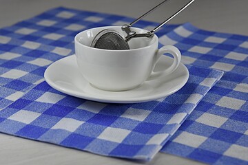 teaspoon in a white cup of tea on a table on a blue checkered napkin