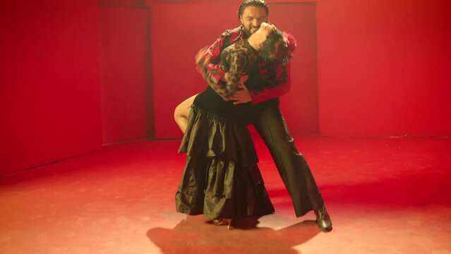 Beautiful couple dancing latin dance . Professional dancers dancing flamenco, rumba or salsa on red background. Couple in spanish dress performs dance movement. Shot ARRI ALEXA Cinema Camera .