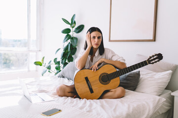 Puzzled brunette female is sad that she can't play guitar. Young woman can’t do hobby with musical instrument because of headache. Bad mood, depression and apathy