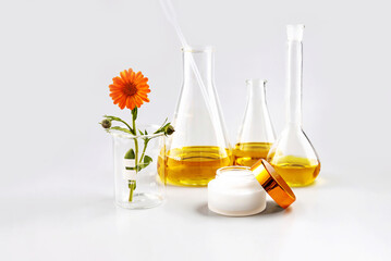 cosmetic containers, laboratory flasks and a calendula flower on a gray background