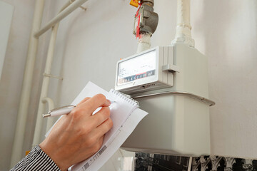 Woman's hand writing down the consumption reading of natural gas at home. Domestic gas meter. 
