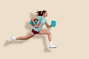 A teenage girl runs to school. In the hands of a backpack and notebooks. Solid beige background