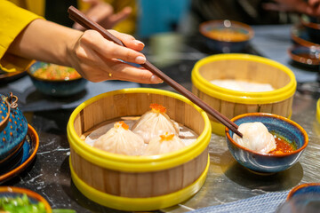 Woman eating Chinese steamed dumpling and steamed pork bun in a bamboo steamer with chopstick. Selective focus.