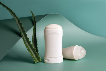 Roll on antiperspirant and solid deodorant near two fresh aloe leaves against teal blue wavy...