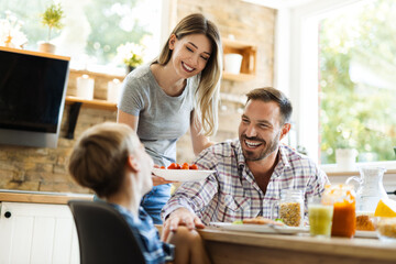 Happy mother serving food to her family while father and son having fun in dining room