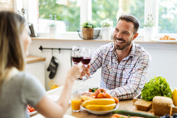 Happy young couple toasting with red wine while having lunch in dining room