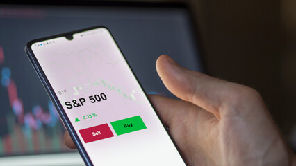 Un investisseur analyse un fonds etf s&p 500 sur un graphique. Un téléphone affiche le cours de l'ETF S&P 500